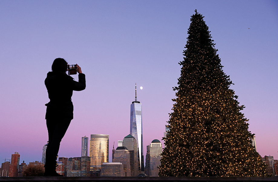 Ein Mädchen macht ein Foto von einem Weihnachtsbaum mit New York im Hintergrund.