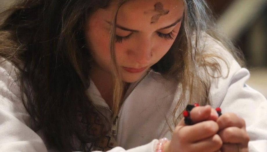 Niña reza tras rexcibir la ceniza.